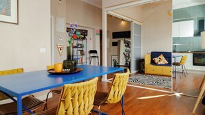 A modern interior with a blue dining table, yellow chairs, a sofa, and a kitchen area. - Loft Pop-Industrial con vista Acquedotto (Rome)