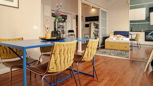 A modern interior with a blue dining table, brown upholstered chairs, a sofa, and a kitchen area. - Loft Pop-Industrial con vista Acquedotto (Rome)
