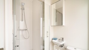 Een moderne badkamer met een glazen douchecabine, een wit wastafeltje en een toilet.