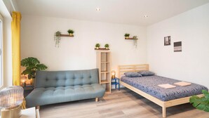 Een slaapkamer met een bank, een bed, een nachtkastje, een lamp, een plank met planten en een wandplank.