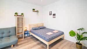 Een slaapkamer met een bed, een bank, een nachtkastje, een lamp en een potplant.