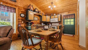 A cozy cabin-style kitchen with wooden walls, a dining table with chairs, and a green door. - American Gem- Charming 2 bedroom cabin all on 1 level & Pet Friendly (Sevierville)
