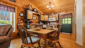 A cozy cabin-style kitchen with wooden walls, a dining table with chairs, and a green door. - American Gem- Charming 2 bedroom cabin all on 1 level & Pet Friendly (Sevierville)