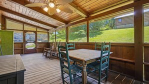 A wooden deck with a table and chairs, large windows, and a ceiling fan. - American Gem- Charming 2 bedroom cabin all on 1 level & Pet Friendly (Sevierville)