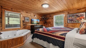 A cabin-style bedroom with a large bed, a wooden ceiling, a bathtub, and a painting on the wall. - American Gem- Charming 2 bedroom cabin all on 1 level & Pet Friendly (Sevierville)