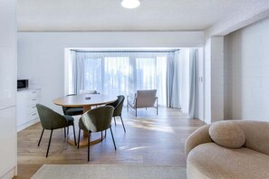 Ein modernes Wohnzimmer mit einem runden Esstisch, vier Stühlen, einer Couch und einer Küchenzeile mit weißen Schränken und einer Mikrowelle.