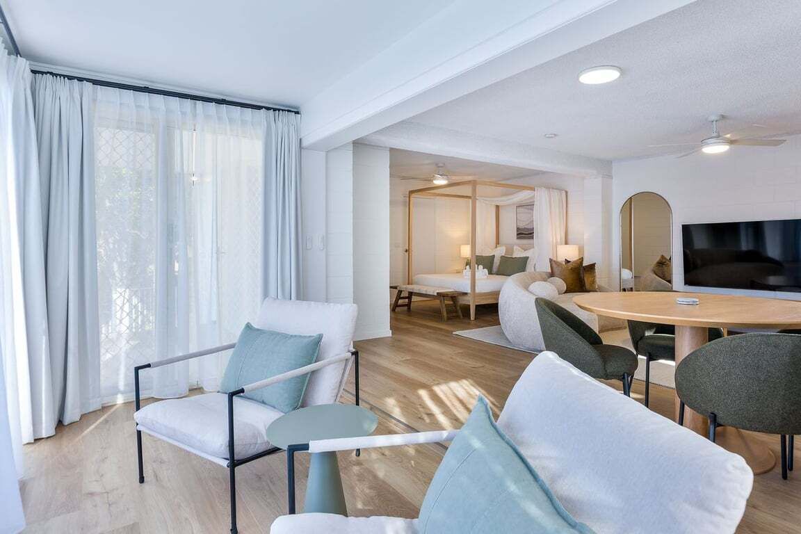 A modern hotel room with a dining area, a large mirror, and a flat-screen TV.