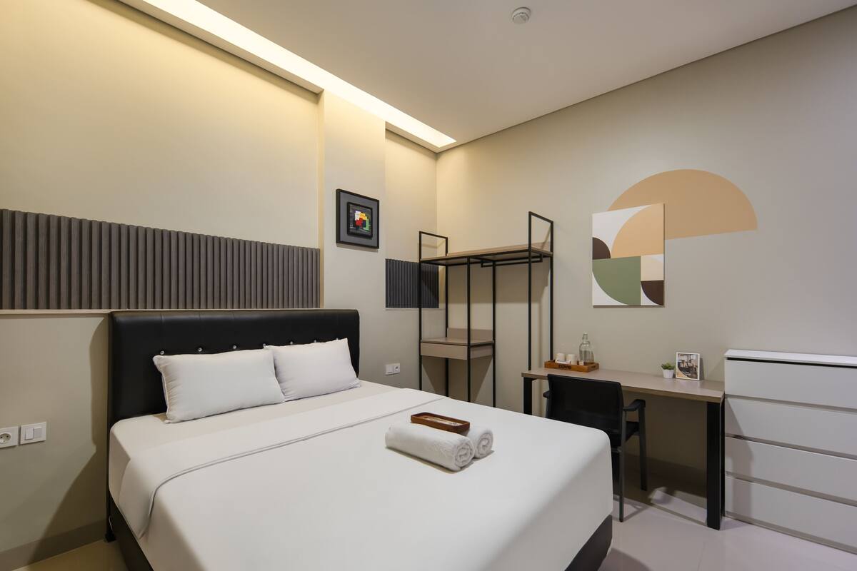 Habitación de hotel con cama, escritorio, silla y televisor en la pared.
