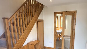 Un escalier en bois mène à une pièce dotée d’une porte, d’un petit banc en bois et d’un plancher recouvert d’une moquette.