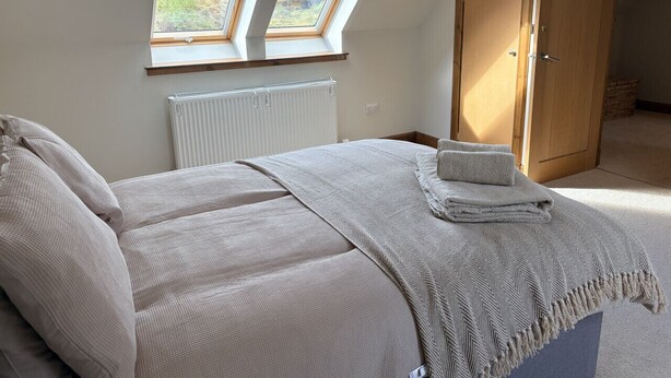 Une chambre à coucher avec un lit, deux fenêtres de toit, un radiateur et une porte en bois.