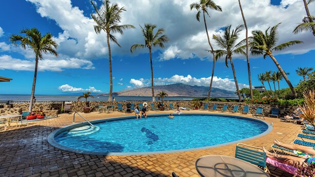 A pool area with lounge chairs, a pool, palm trees, and a view of the ocean. - Oceanfront Menehune Shores #206, Lanai Views, Pool, Steps to Beach, Relax in Kihei (Kihei, Maui)