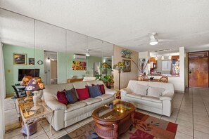 A living room with two white sofas, a glass coffee table, and a ceiling fan. - Oceanfront Menehune Shores #206, Lanai Views, Pool, Steps to Beach, Relax in Kihei (Kihei, Maui)