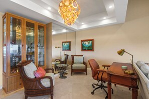 A room with a dining table, chairs, a cabinet with glass doors, a sofa, and a chandelier. - Luxury Oceanfront 3-Bedroom Escape at Makena Surf Resort - Makena Surf #E-304 (Makena, Maui)