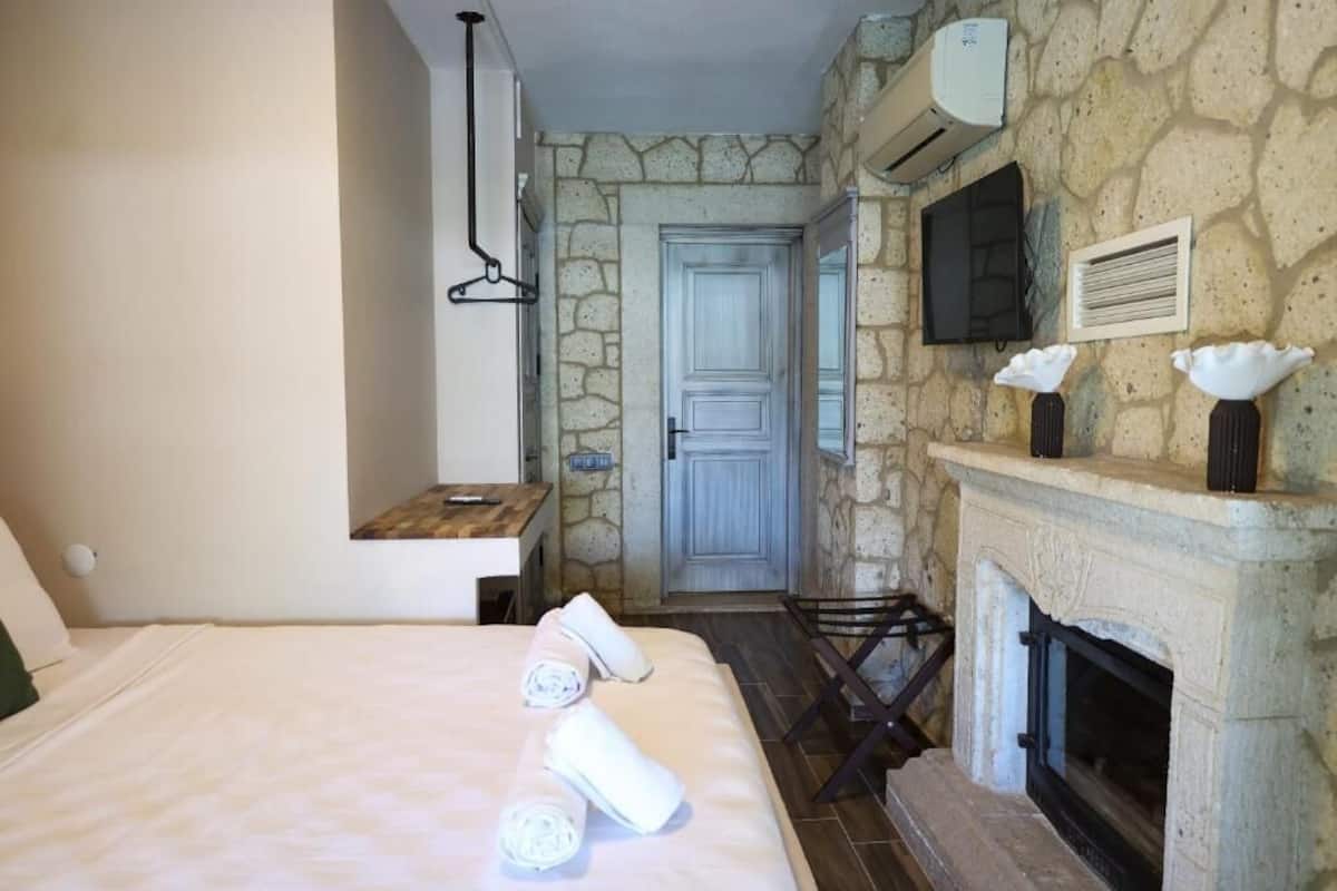 A bedroom with a stone wall, a fireplace, a bed with towels, a wooden bench, and a door.