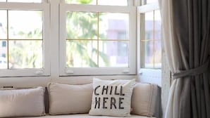 Una habitación con asiento junto a la ventana, una toalla enrollada y un cojín con la inscripción 'CHILL HERE'.