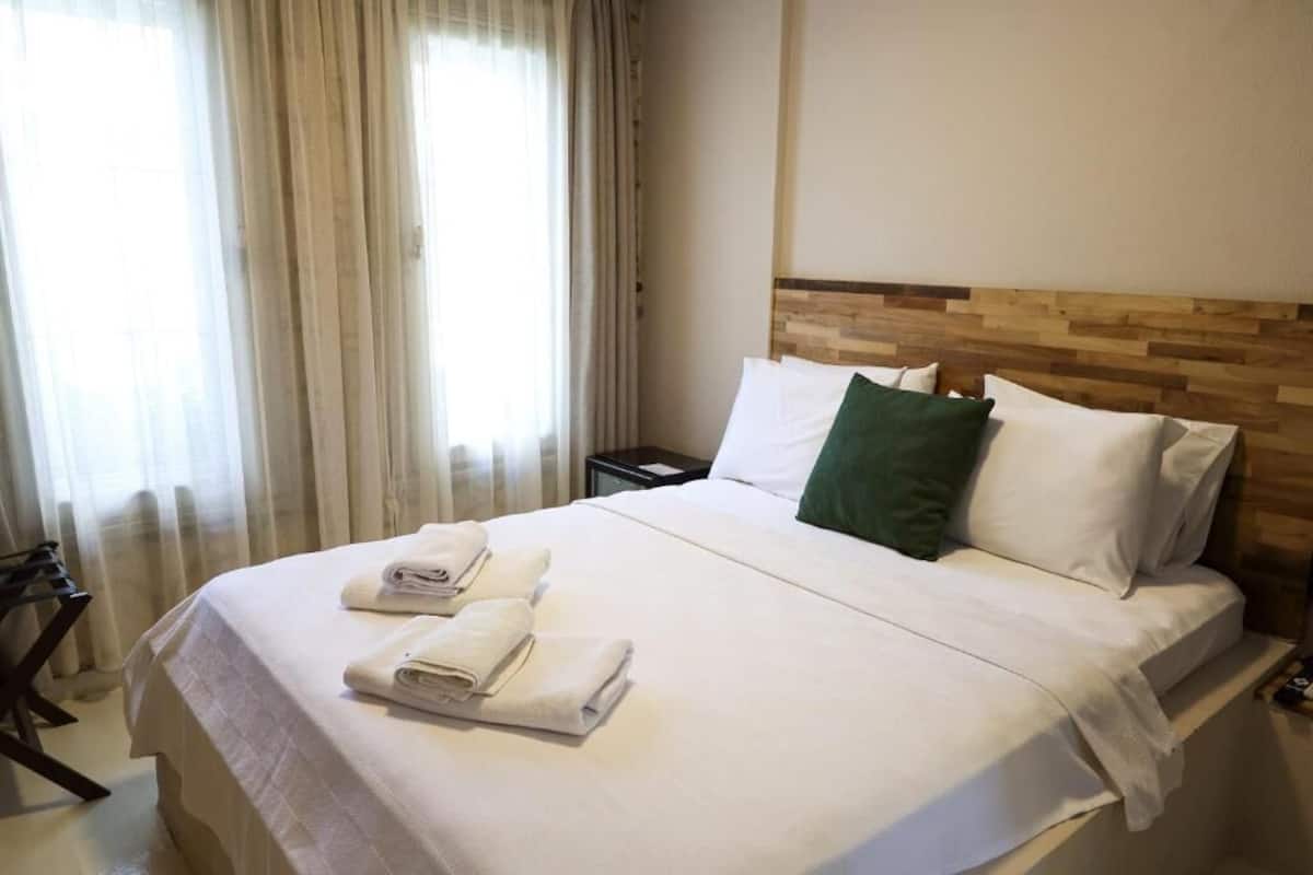 A hotel room with a bed, a wooden headboard, a nightstand, and a window with curtains.