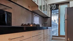 A kitchen with a black countertop, wooden cabinets, a stainless steel refrigerator, and a window with a view of buildings.