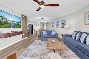 A modern living room with a flat-screen TV, a ceiling fan, a sofa, a coffee table, and a dining area.