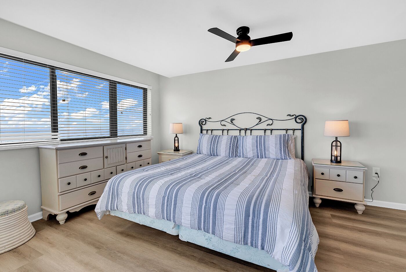 A bedroom with a bed, nightstands, a ceiling fan, and a window with blinds.