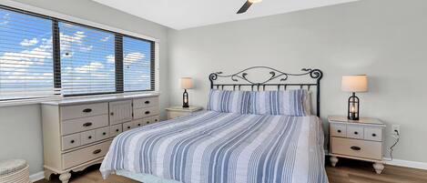 A bedroom with a bed, nightstands, a ceiling fan, and a window with blinds.