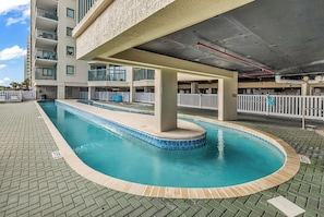 A swimming pool with a tiled edge, located under a building with balconies and a covered area.