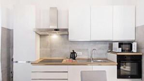 A modern kitchen with white cabinets, a stainless steel sink, a microwave, and an oven. - Castle Suite – Welcoming comfort in the heart of Cagliari ✨ (Cagliari)