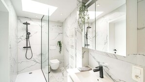 A modern bathroom with a glass shower enclosure, a white toilet, and a large mirror.