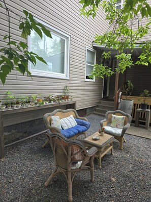 Eine Terrassenfläche mit Korbmöbeln, einer Bank und Blumentöpfen.