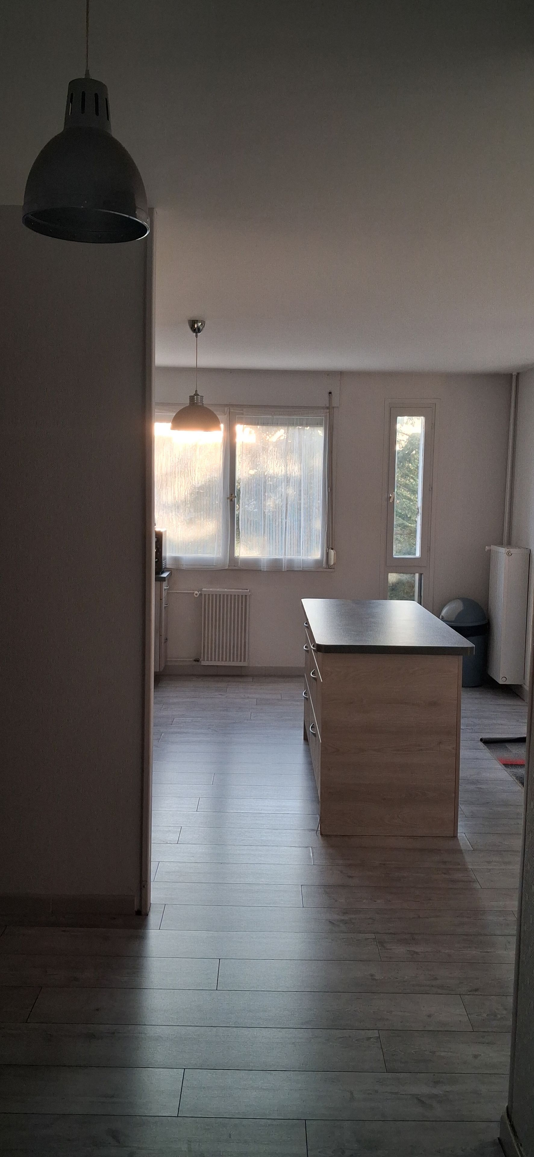 A spacious room with a large wooden table, a hanging light fixture, and a window with curtains.
