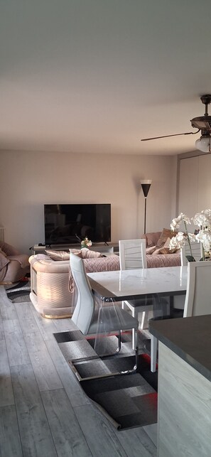 A modern living room with a dining area, a flat-screen TV, and a ceiling fan. - Large, Entire Apartment Near Paris (Creil)