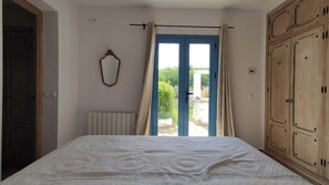 Une chambre à coucher avec un lit, une fenêtre avec des rideaux, un radiateur, un miroir et des armoires en bois.