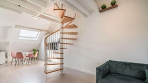 Un interior moderno con una escalera espiral, un sofá verde y un comedor con sillas rosas.