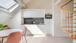 Una cocina moderna con armarios blancos, encimera negra y escalera de madera.