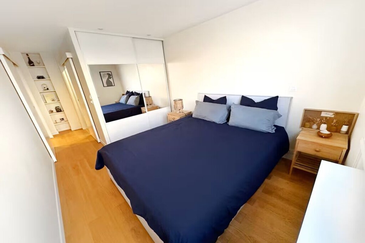 A bedroom with a large bed, a wardrobe, a bedside table, and a mirror.