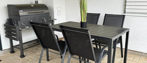 An outdoor patio with a grill, a table, and chairs.