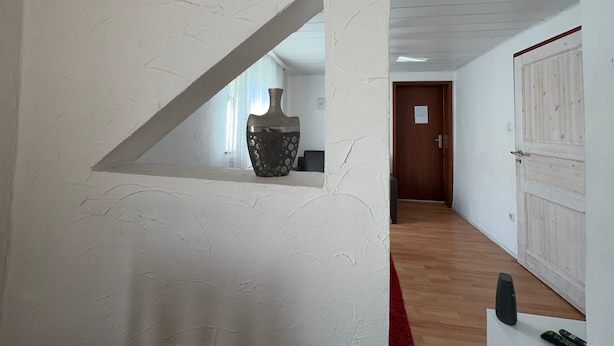 A hallway with a white wall, a wooden door, a red carpet, and a vase on a shelf. - Apartment 'Liki' with Wi-Fi (Siegen)