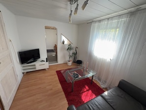 Een woonkamer met een televisie, een glazen salontafel, een rood vloerkleed, een bank en een trap naar een andere kamer.