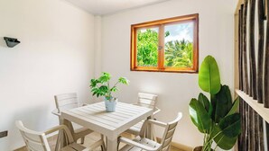 A dining area with a white table and chairs, a potted plant, and a window with a view of greenery.