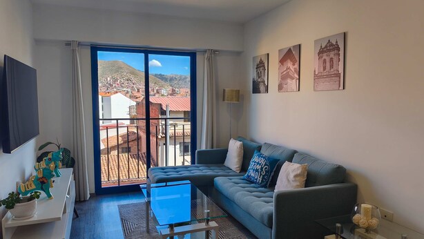 A modern living room with a sofa, a glass coffee table, a TV, and a balcony with a city view. - w Dreamy 2BR w Private Balcony in Cusco (Cusco)