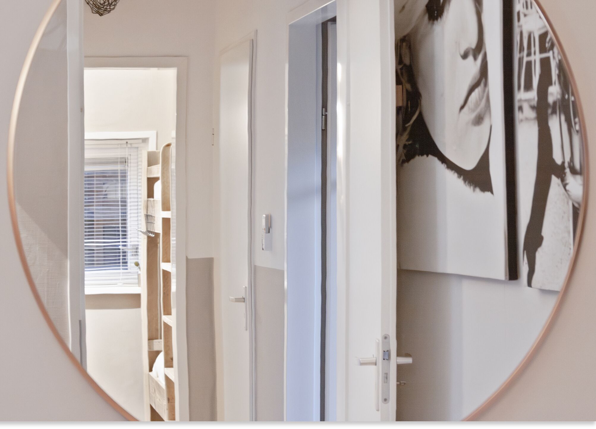 Een gang met een deur naar een kamer, een raam met jaloezieën en een muur met een lijstwerkfoto.