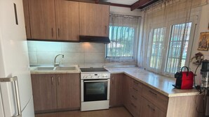 A kitchen with wooden cabinets, a white stove, a sink, and a window with lace curtains.