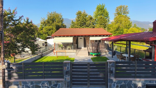 A house with a stone facade, a red roof, and a patio area with a swing set.