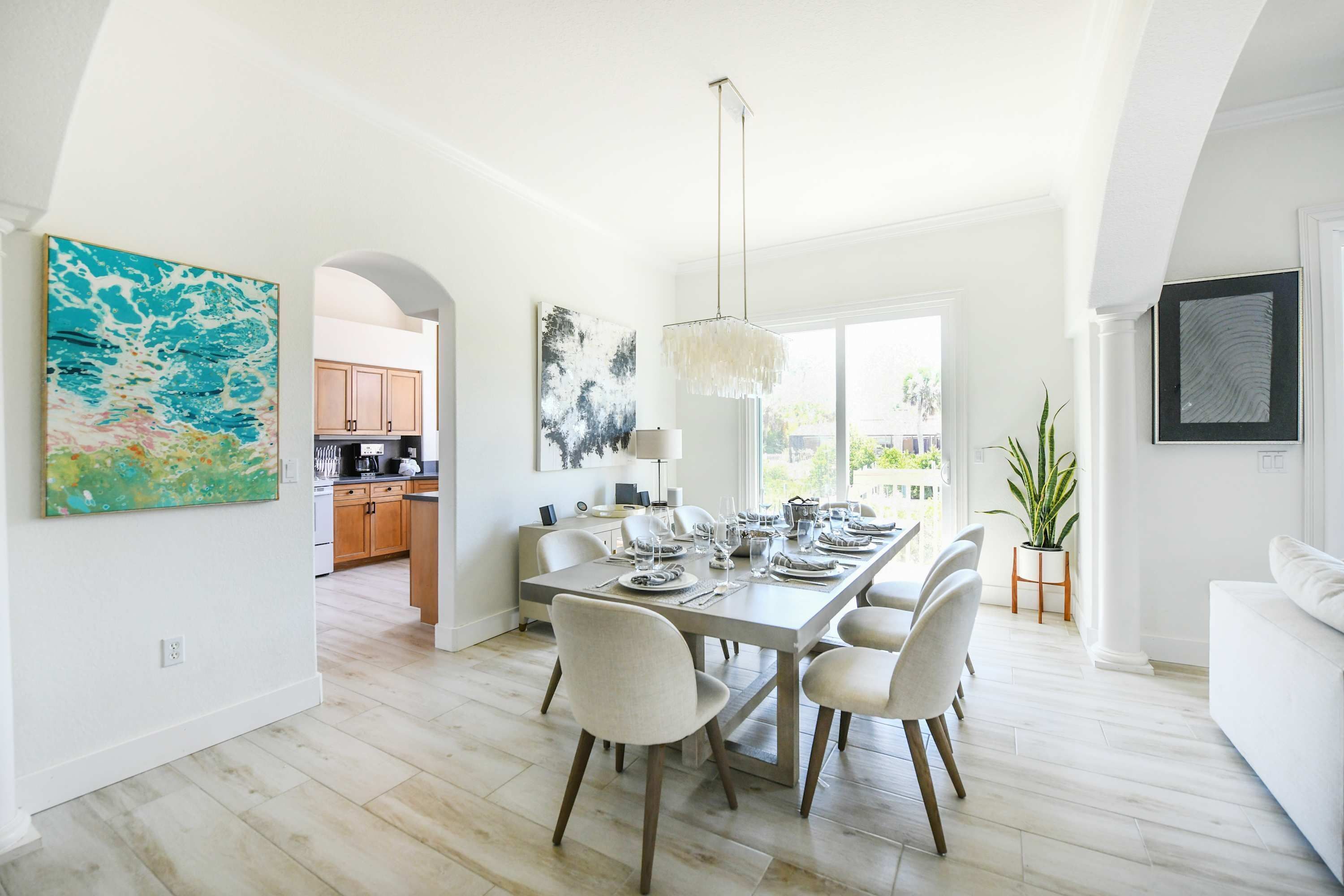 A modern dining area with a long table set for six, a chandelier, and artwork on the walls.