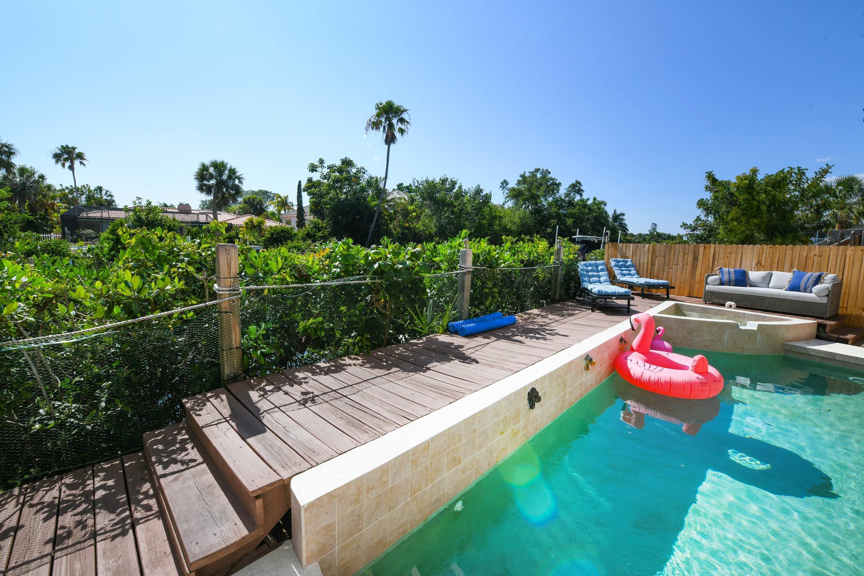 A swimming pool with a wooden deck, lounge chairs, and a pink flamingo float.