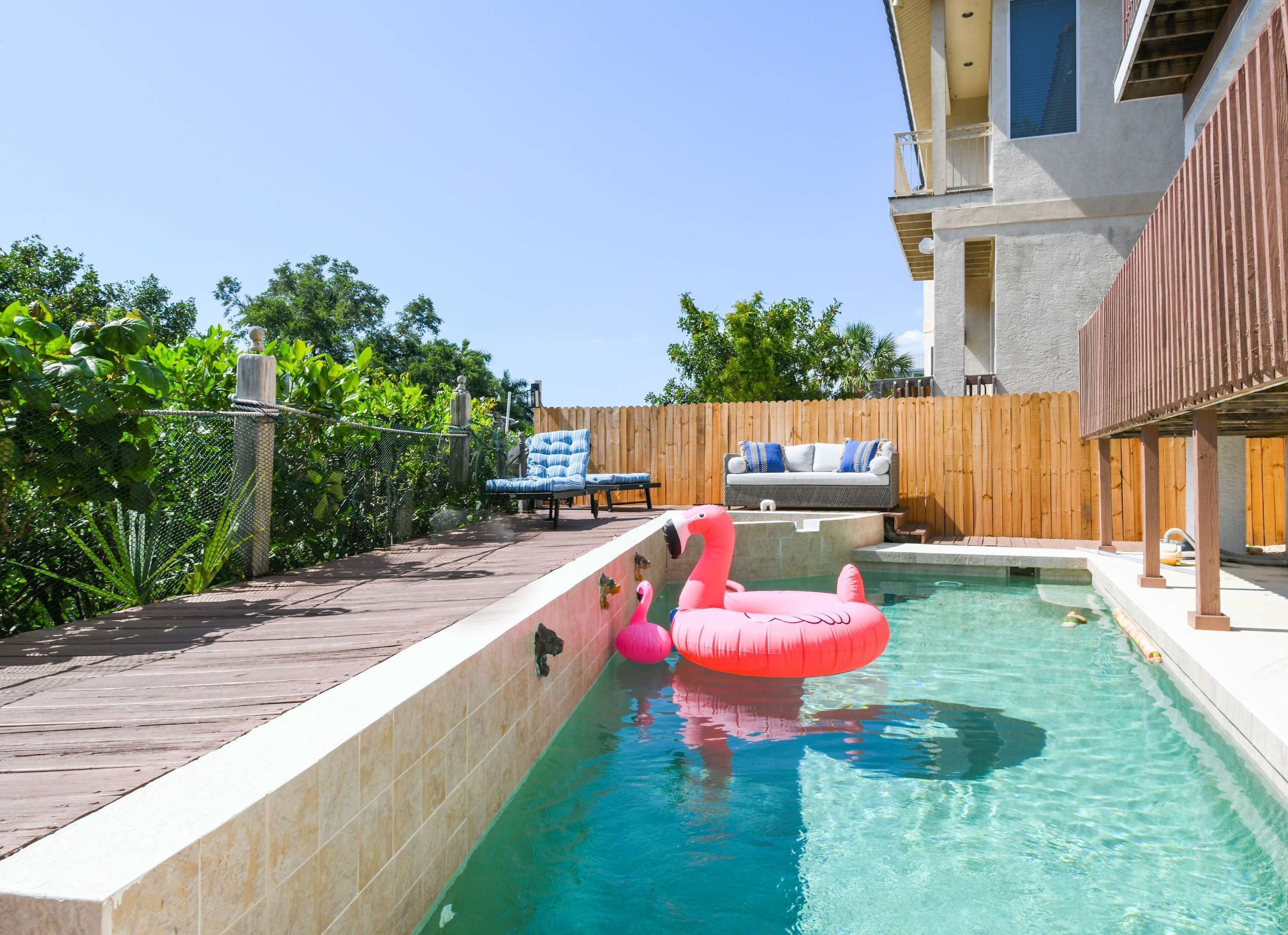 Une piscine avec une terrasse en bois, un fauteuil de relaxation et un flotteur en forme de flamant rose.