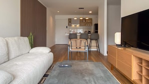 Ein modernes Wohnzimmer mit einer Couch, einem Couchtisch, einem Fernseher und einer Küche im Hintergrund.