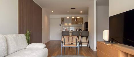 A modern living room with a sofa, a coffee table, a TV, and a kitchen in the background.