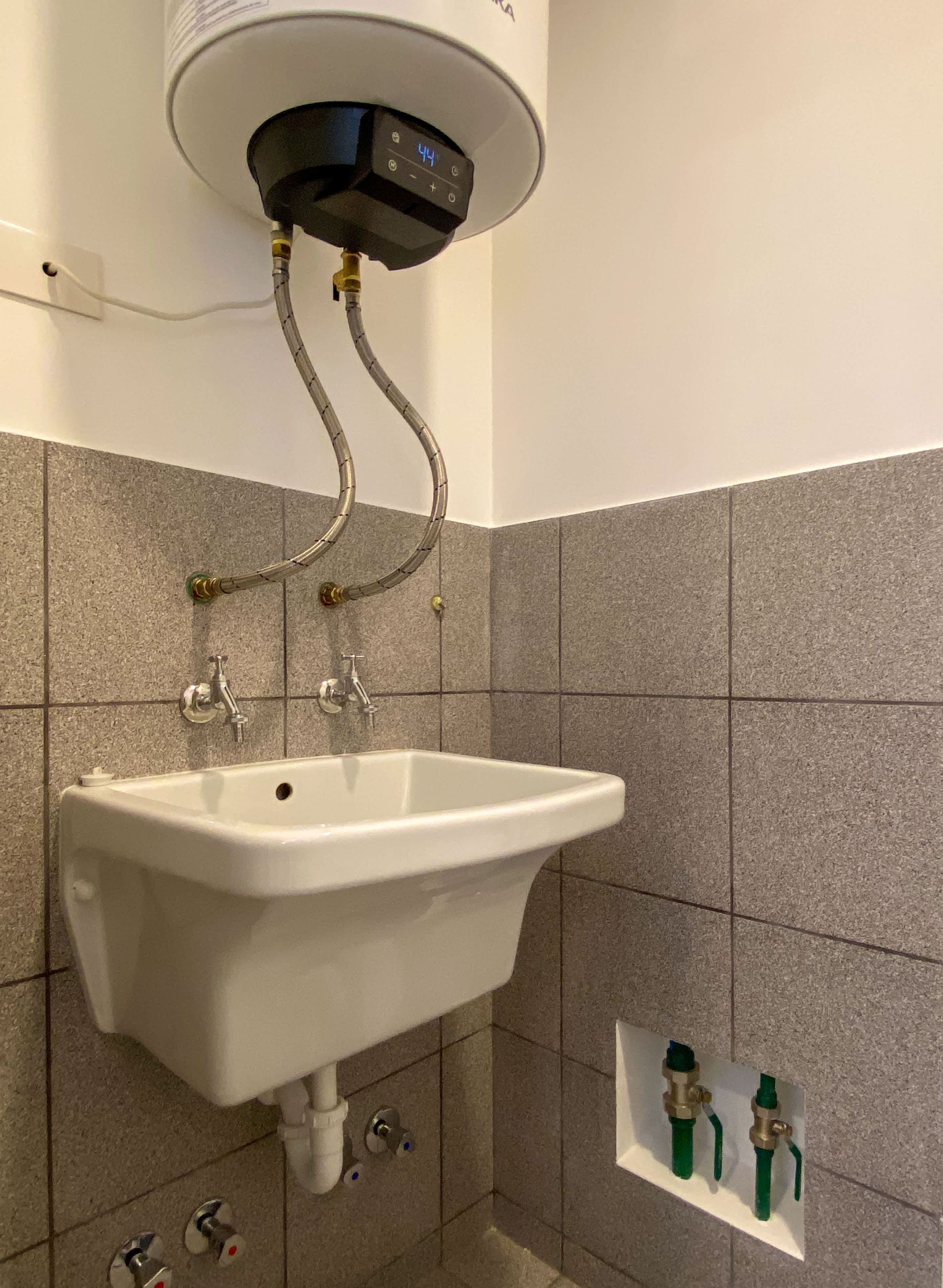 A bathroom with a white sink, a wall-mounted heater, and two green faucets.