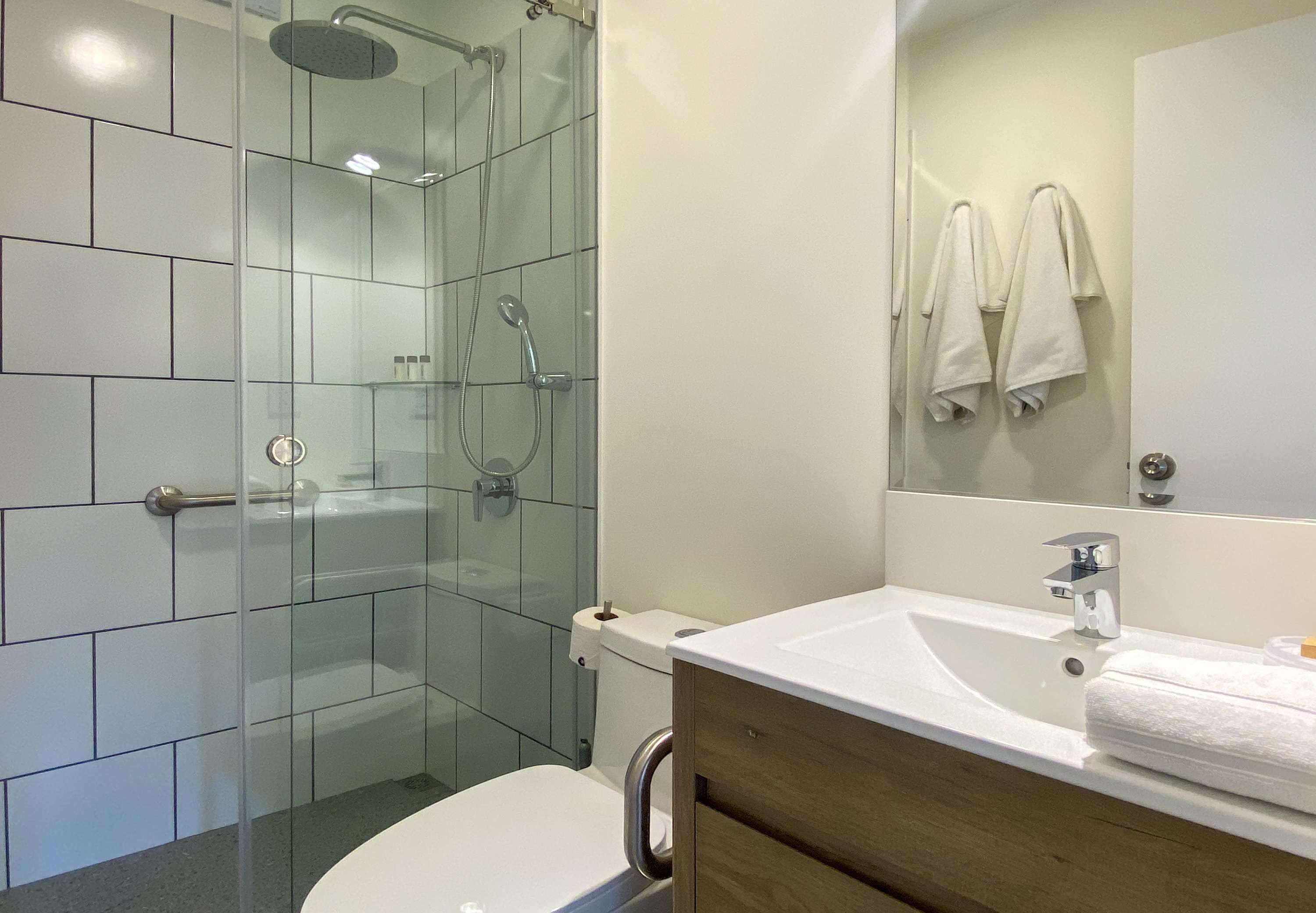 A modern bathroom with a glass-enclosed shower, a white sink, and a mirror with towels.
