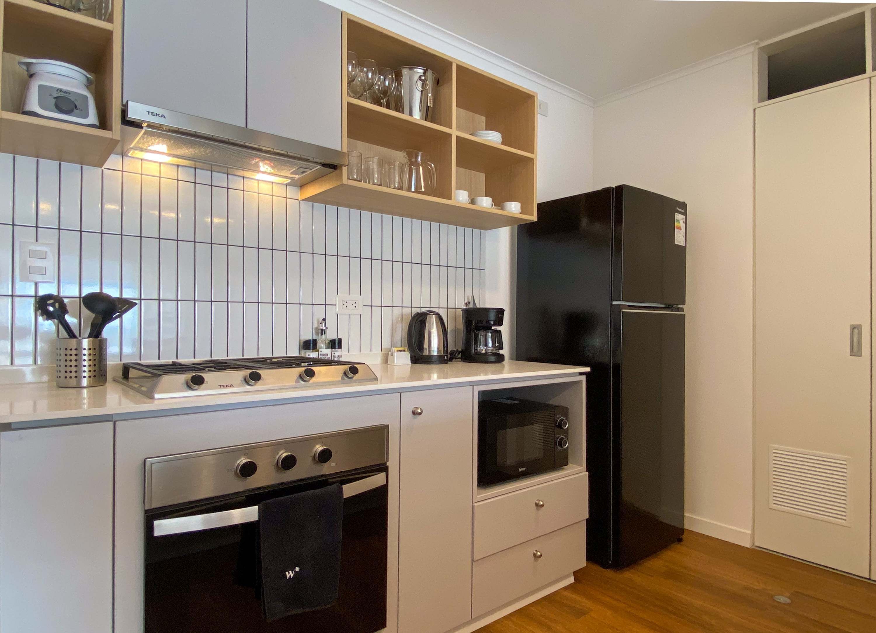 A compact kitchen with a gas stove, oven, microwave, and a black refrigerator.